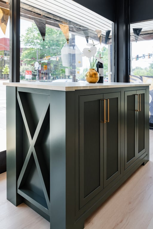 A dark green kitchen island with a marble countertop and detailed cabinetry in our Bethesda showroom