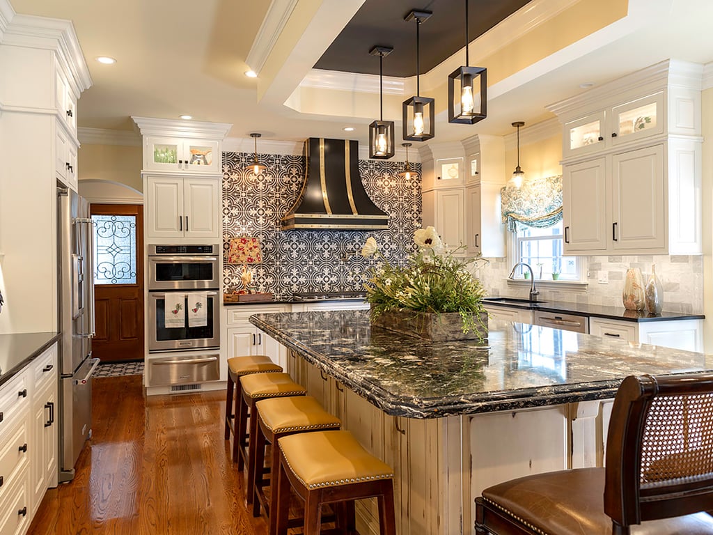Spacious kitchen with white cabinets, a patterned tile backsplash, black range hood, a large island with dark marble countertop, and pendant lights