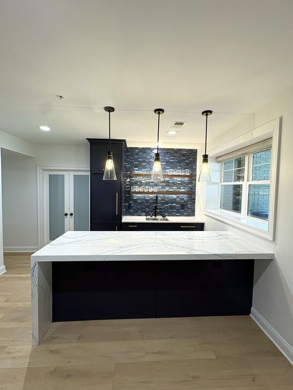 Finished basement wet bar with a waterfall marble countertop, dark cabinetry, and pendant lighting