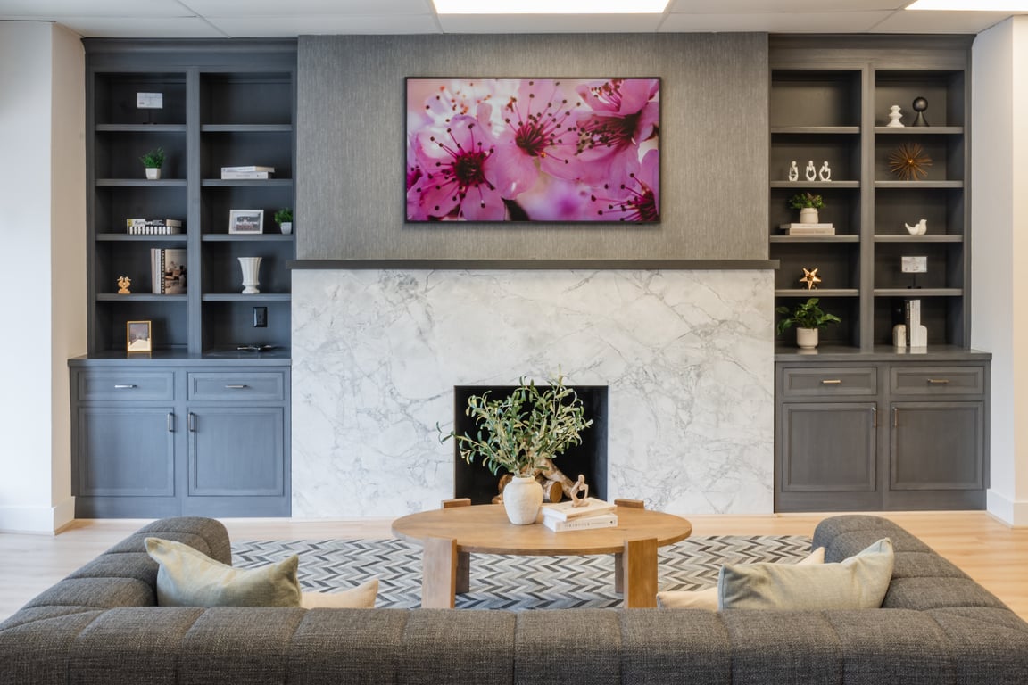 Modern living room with gray sofa, wooden coffee table, marble fireplace, built-in shelves, and a TV displaying pink cherry blossoms