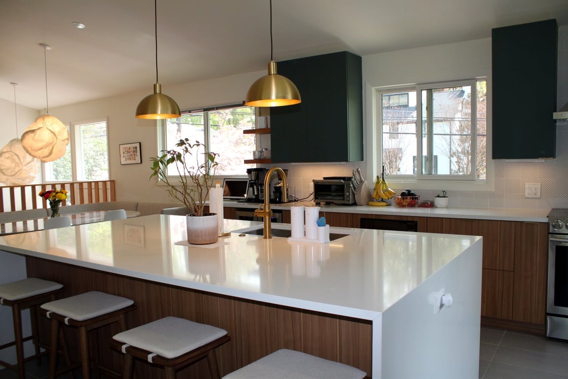 Open-concept main floor with a vaulted, skylit kitchen — green cabinetry, a large white island, and gold pendant lights