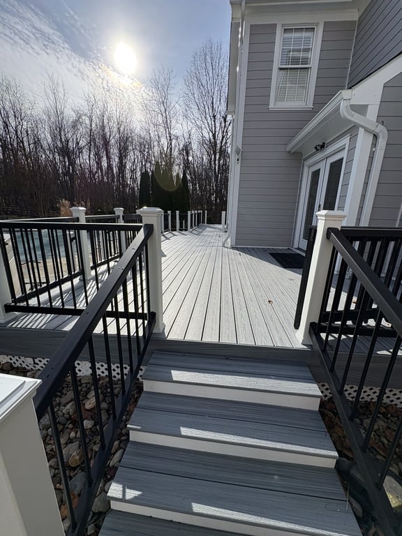 A finished composite deck with gray decking and black metal railings under a blue sky