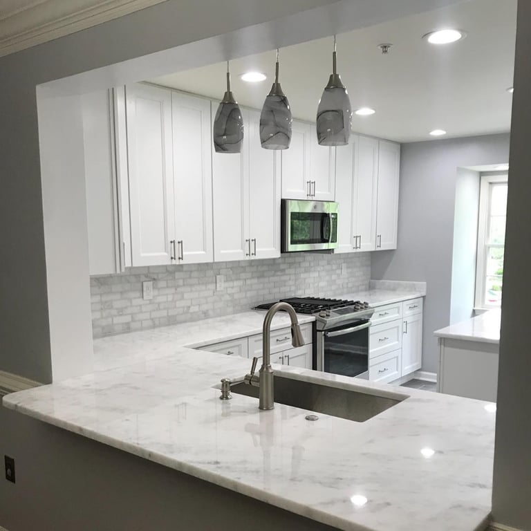 Modern kitchen with white cabinets, marble countertops, gray subway tile backsplash, stainless steel appliances, and three pendant lights above the island