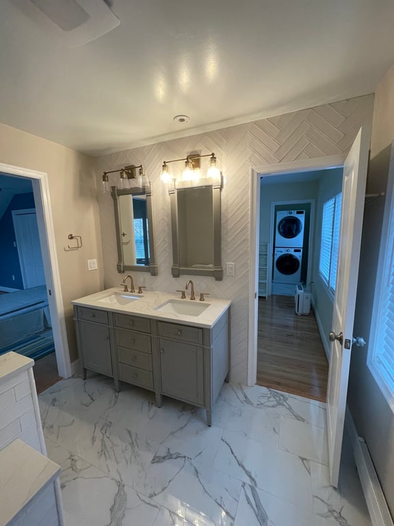 Modern bathroom with double gray vanity, two mirrors, two brass faucets, and white marble floor