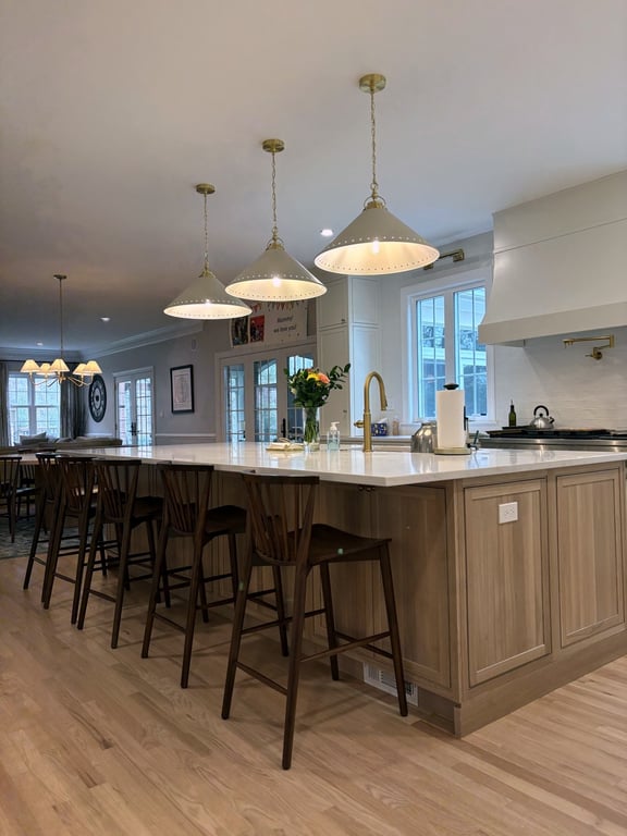 Warm transitional kitchen with a large island, counter stools, gold pendant lights, and bright windows