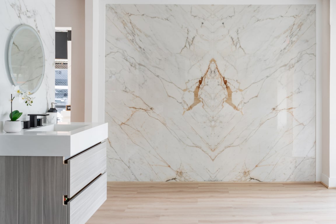 Bright bathroom with a book-matched Calacatta marble slab feature wall, floating vanity, round mirror, and light wood floor