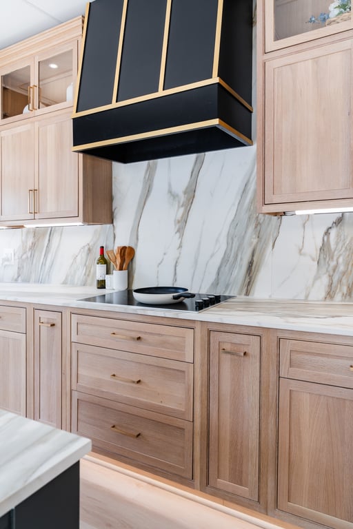 Modern kitchen with light wood cabinets, marble backsplash and countertop, and a black and gold range hood