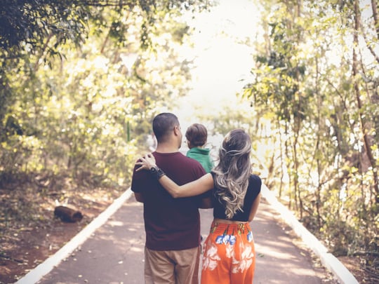 Young family walking in a light forest and carrying their toddler