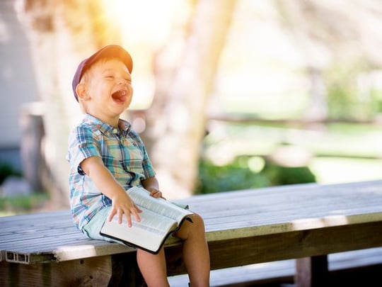 Boy sitting with book on a bench and laughing