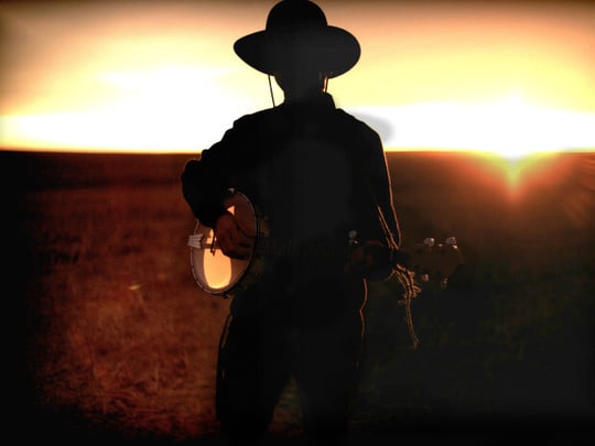 Silhouette of a person wearing a cowboy hat and playing a banjo