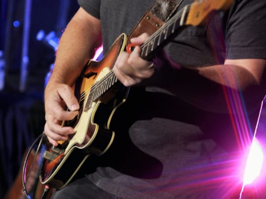 Man in black shirt playing a brown electric guitar
