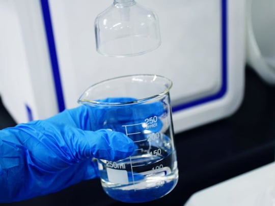 Blue glove holding glass beaker