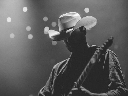 Person wearing a white cowboy hat playing on a lit stage
