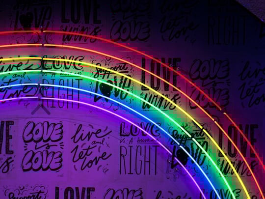 A neon rainbow sign with black writing behind it