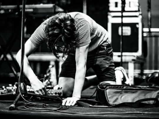 Black and white image of a person plugging in a pedalboard on stage