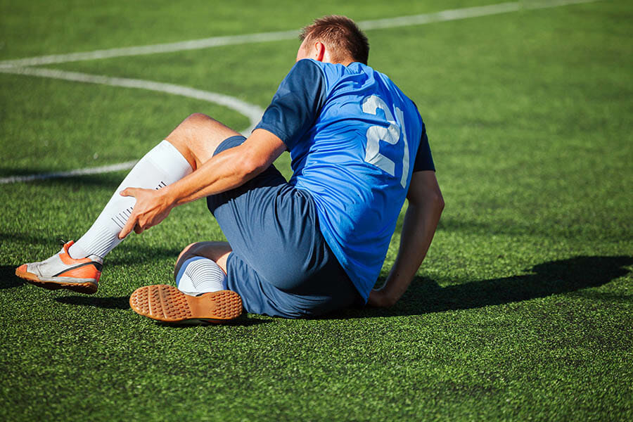 sport, football training, sports injury and people - injured soccer player with ball on field