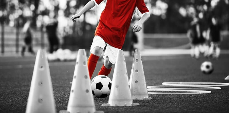 Child dribbling through cones