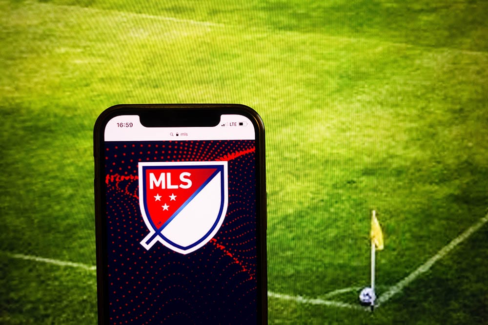Smartphone displaying logo of MLS on soccer stadium background