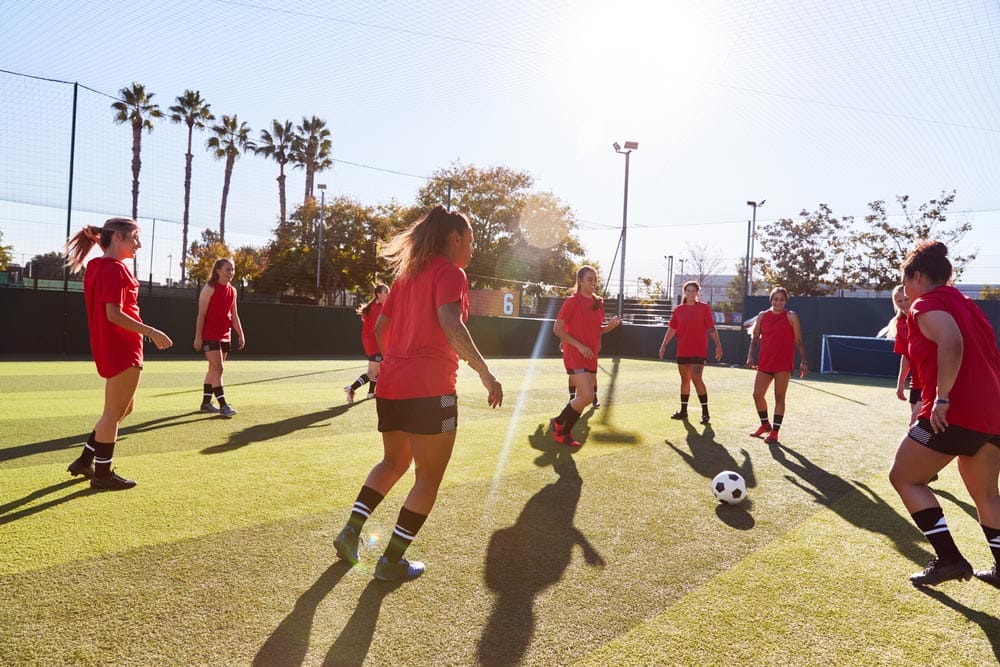 Womens Football Team Kicking Ball Whilst Training For Soccer Match On Outdoor Astro Turf Pitch