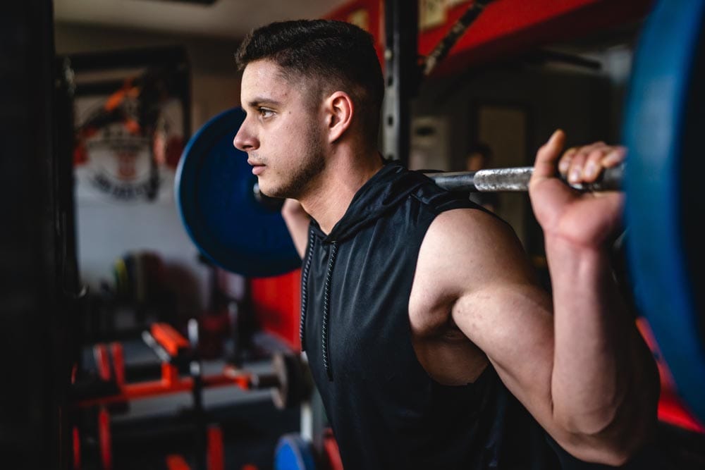 One man training at gym male athlete amateur or sportsman doing squats with barbell and weight on shoulders close up copy space strength and fitness bodybuilding exercise concept
