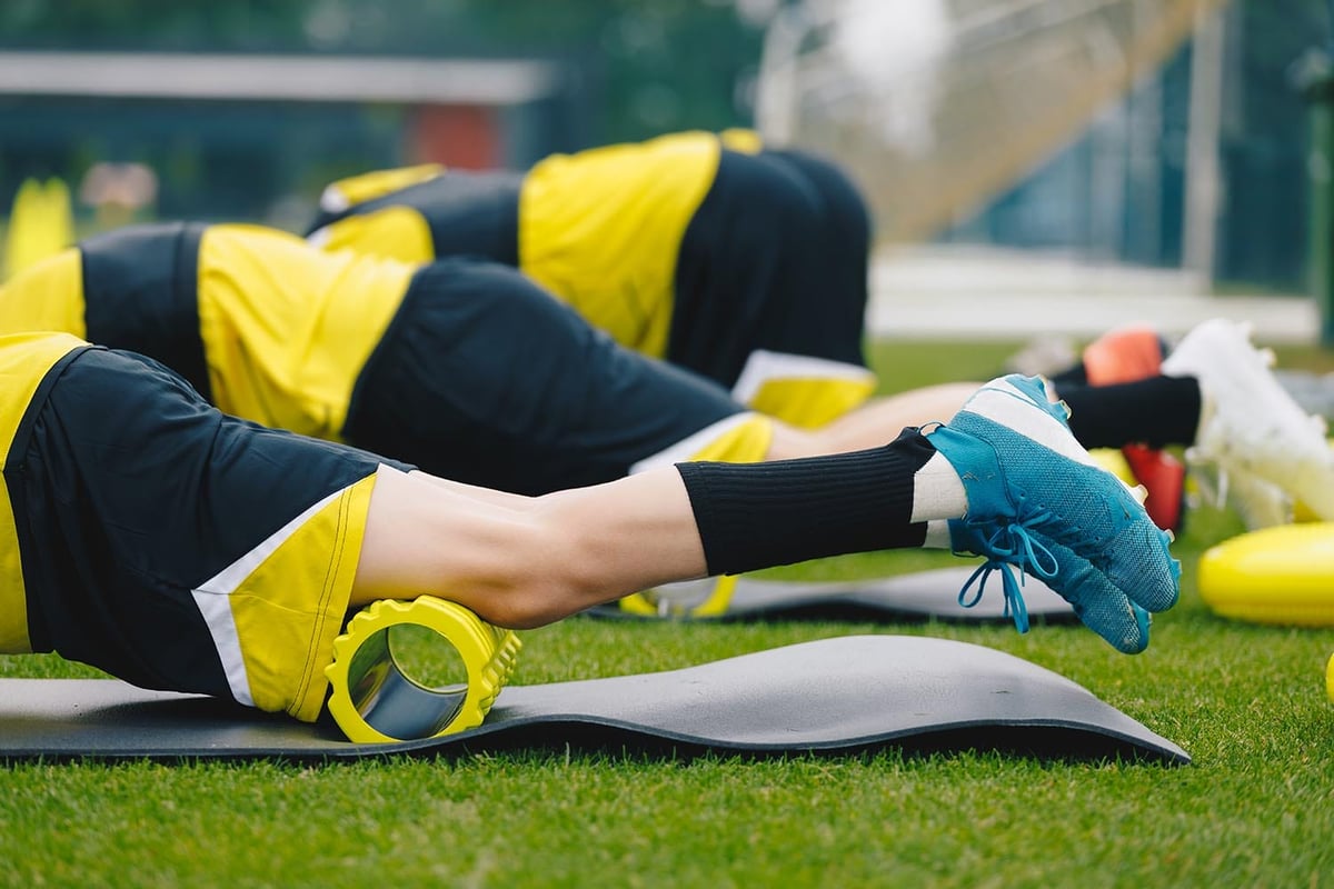 Foam Rolling. Group of Young Soccer Players in Soccer Cleats Using Training Foam Roller on Training Session. Stretching and Warming Up Muscles