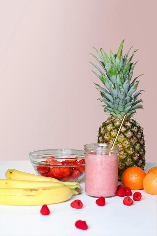a table with fruit on. A pineapple next to a smoothie glass and berries and bananas