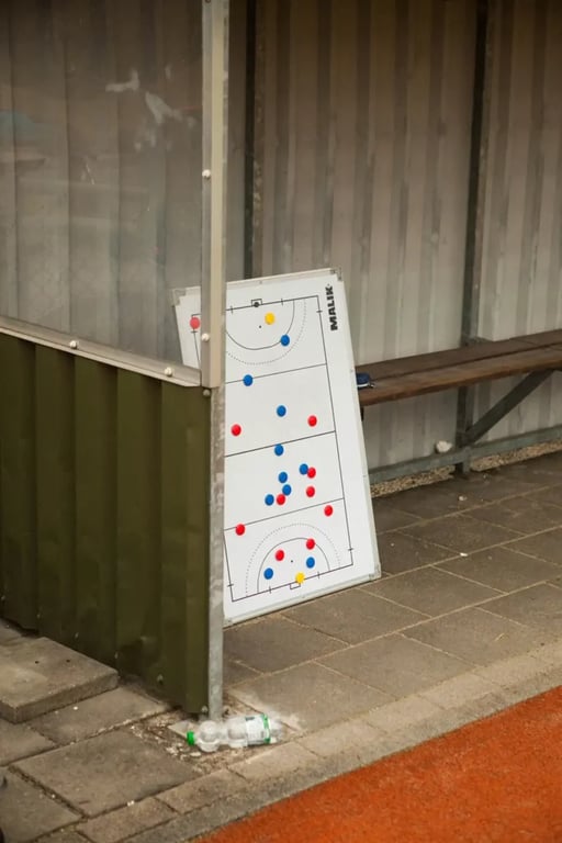 A white board with tactical football markers of red and blue sat on the floor propped up against the shed of a football dugout