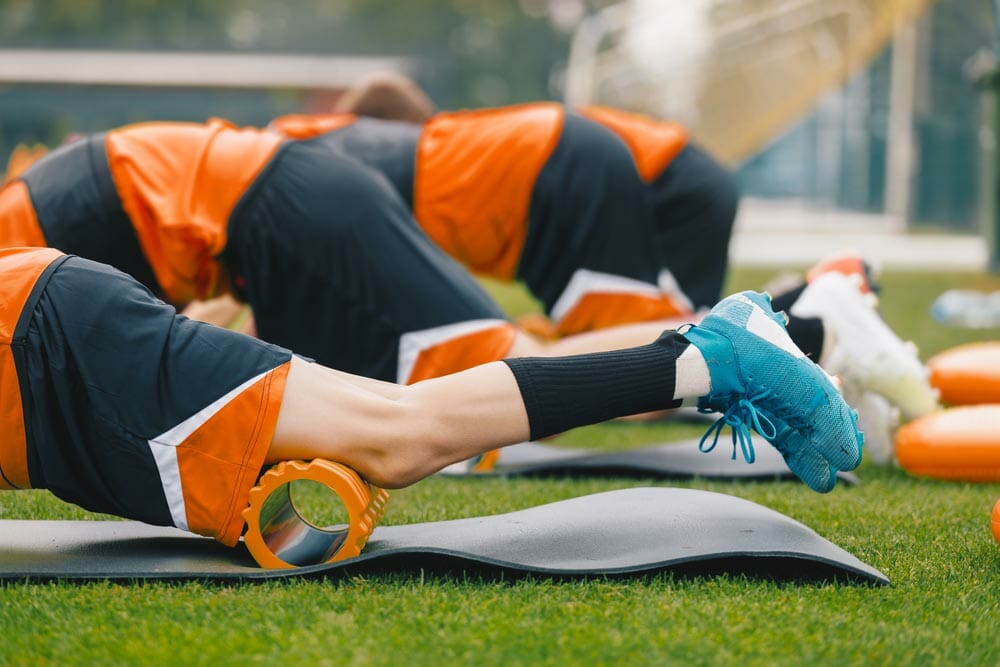 Group of Young Athletes on Stretching Outdoor Session with Foam Rollers and Mats. Soccer Football Players in a Team on Fitness Workout to Relieve Muscle Tightness, Soreness, and Inflammation