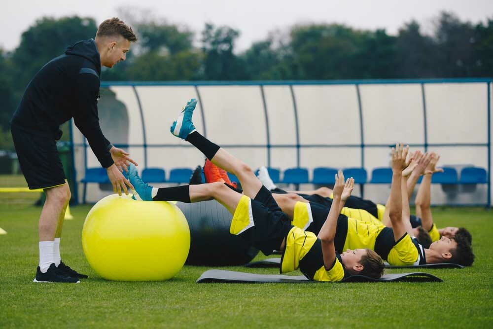 Young Soccer Players in Team on Training with Coach. Boys Training with a Gym Ball. Stability Training On Junior Male Soccer Team. Coach Instructs Players How to Exercise with Gym Balls Properly
