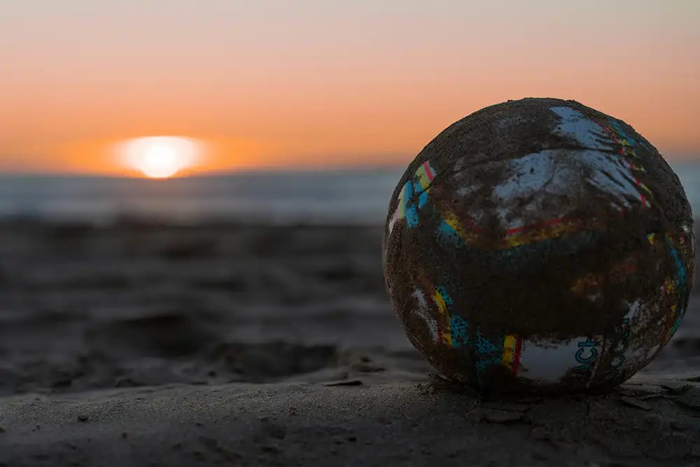 Soccer Ball Covered in Sand on a Beach at Sunset