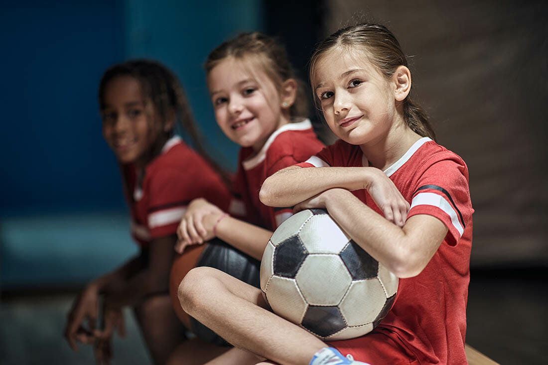 Smiling girl with soccer ball in good mood before training in changing room.