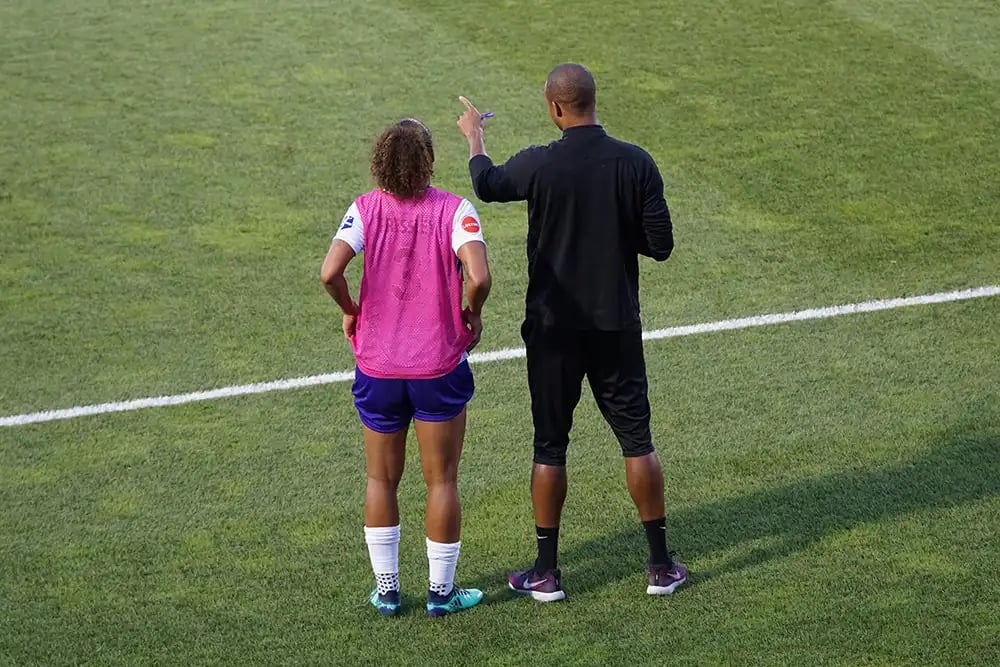 A female footballer on the sidelines next to a referee