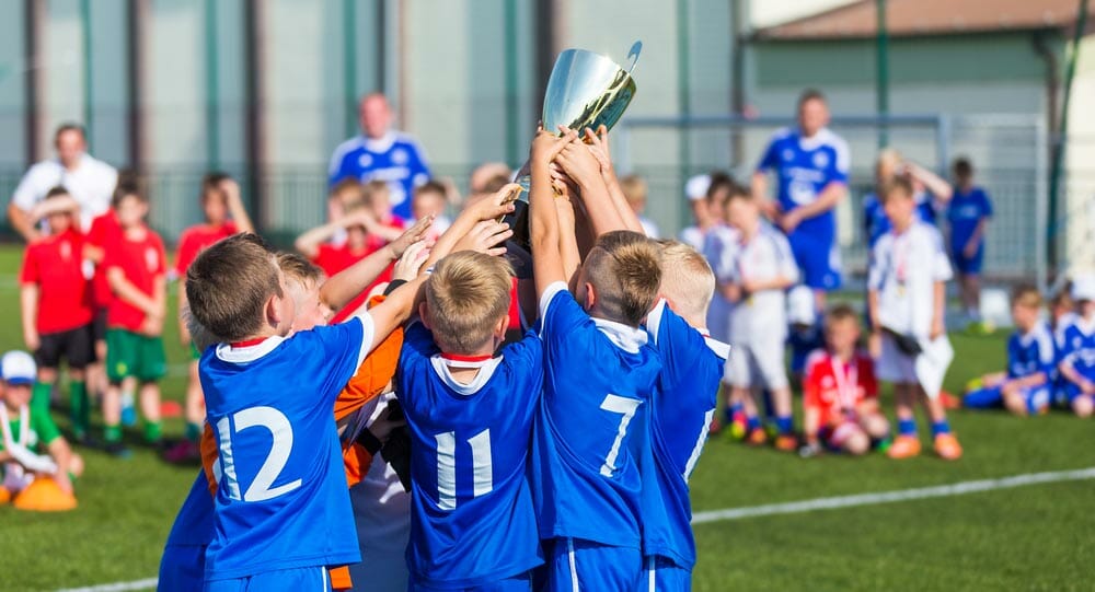Young Soccer Players Holding Trophy. Boys Celebrating Soccer Football Championship. Winning team of sport tournament for kids children. Horizontal sport background.