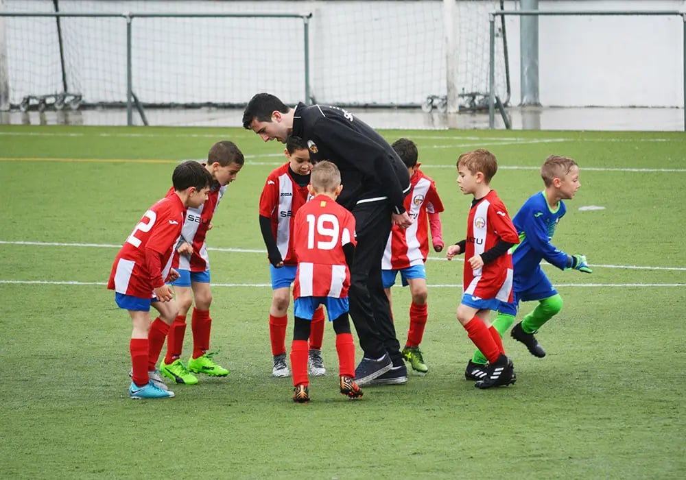 A football coach in a black tracksuit training young children football