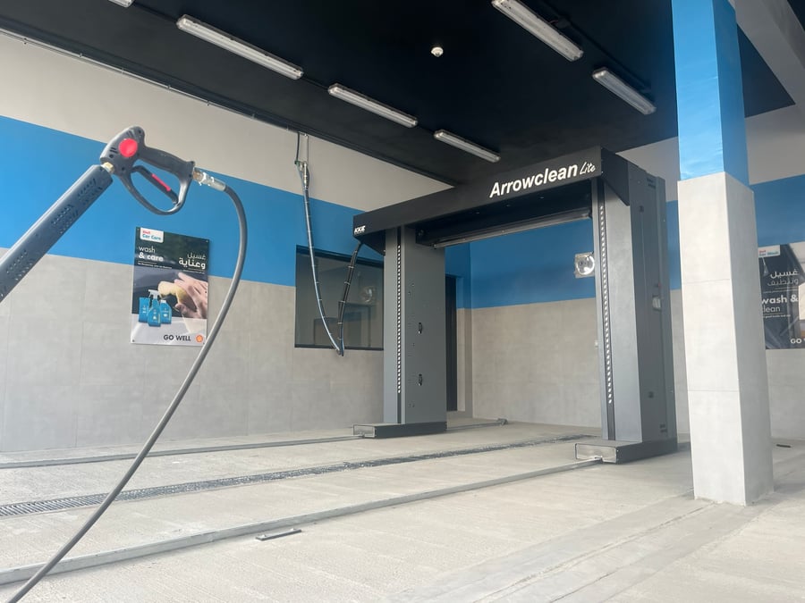 A KKE ArrowClean Lite standing idle on its floor rails in a finished tiled forecourt wash bay, with a coiled high-pressure lance in the foreground