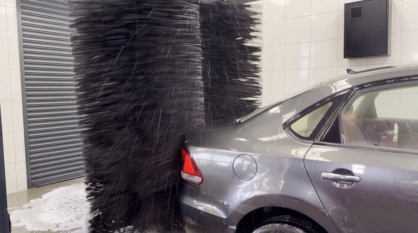 A vertical side brush flared and spinning against the rear flank of a grey saloon