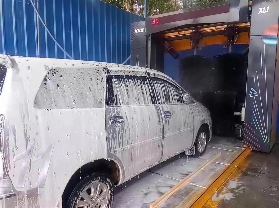 A washed MPV pulling out of a KKE X1.1 bay past the gantry, the yellow floor guide lines running out onto the forecourt