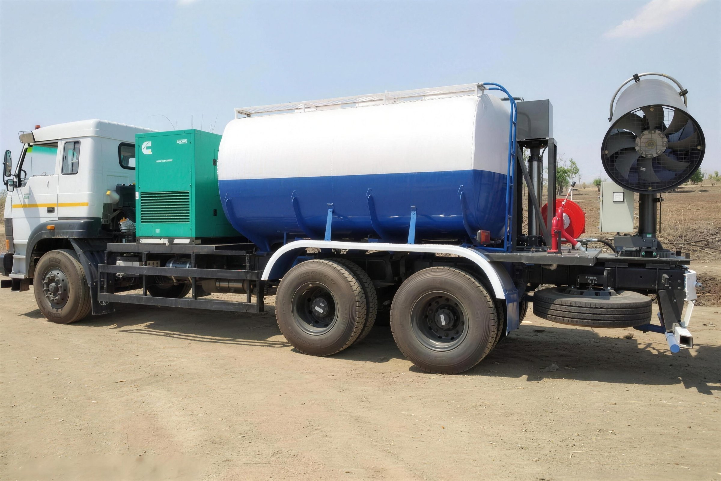 Side profile of a truck-mounted KKE MistBeam: the tanker cab, a Cummins generator set on the deck, the white-over-blue water tank, and the fog cannon on its slew column at the rear beside a red hose reel and water monitor