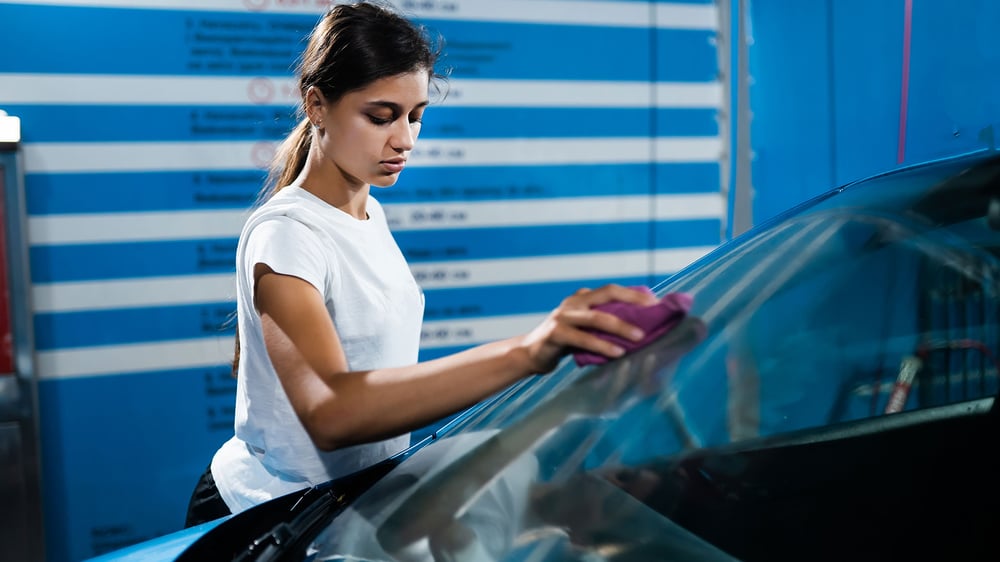 A detailer wiping down a car windscreen with a microfibre cloth