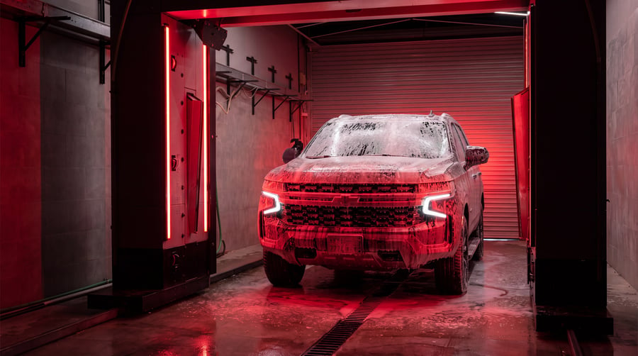 An SUV under full foam in a bay lit red