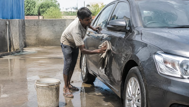A car wash worker wiping a car by hand in a wet yard
