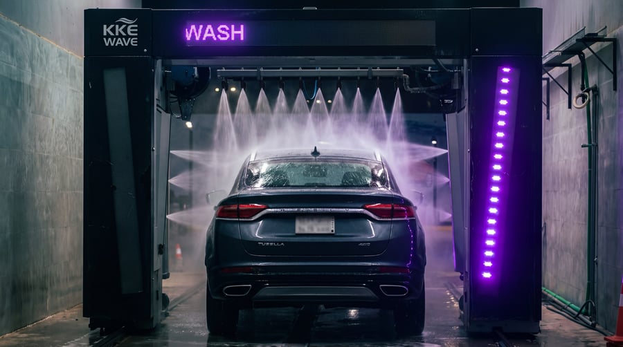 Fans of high-pressure water firing down across the rear of a car inside the wash bay