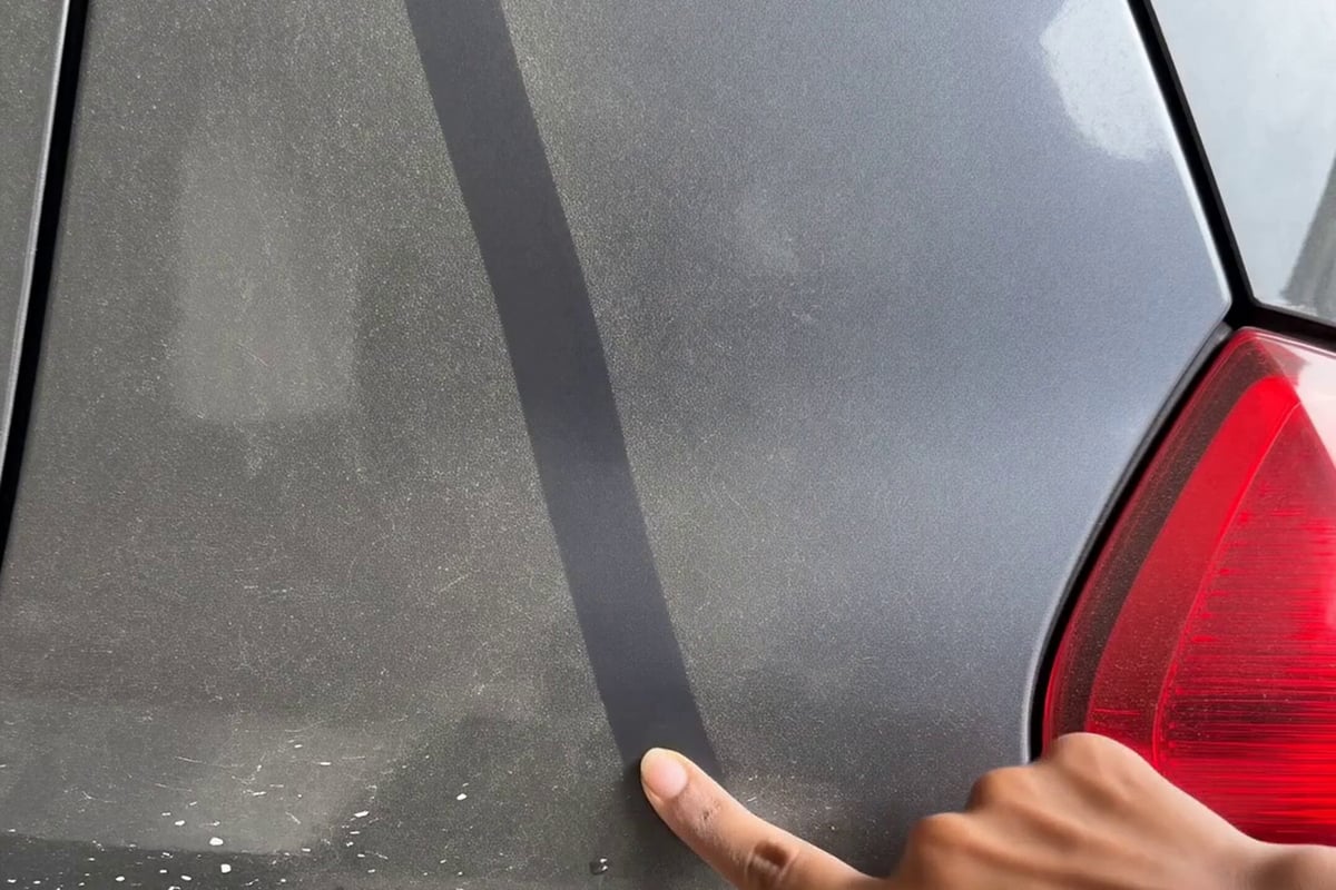The fingertip test: a finger drawn through the dust film on a car's rear panel, leaving a clean line that shows how much dry dust the paint is carrying.