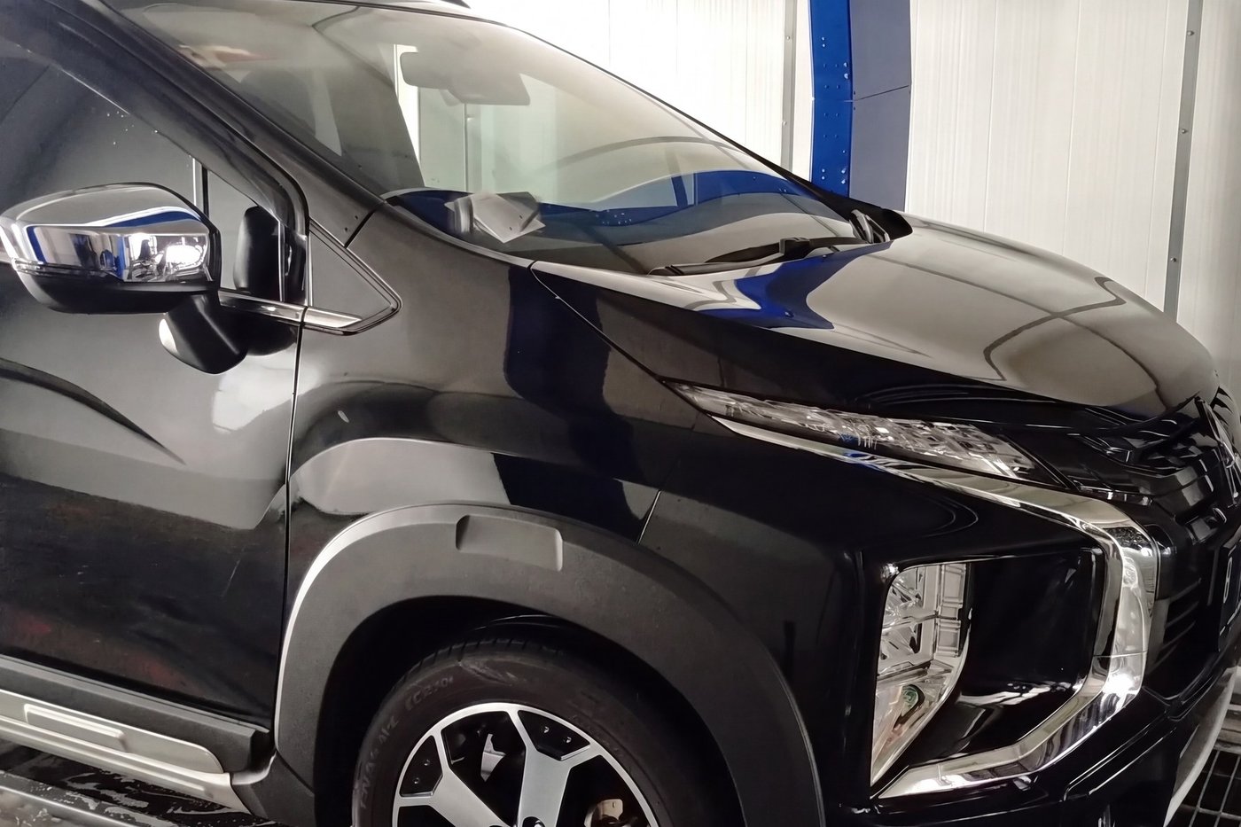 A washed dark MPV standing glossy and clean at the exit of a KKE tunnel car wash, the wet floor and a blue machine column behind it