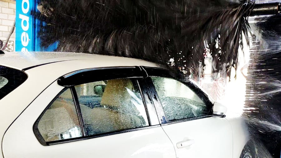 A KKE Speedoclean horizontal brush working across the roof and rear glass of a white hatchback mid-wash