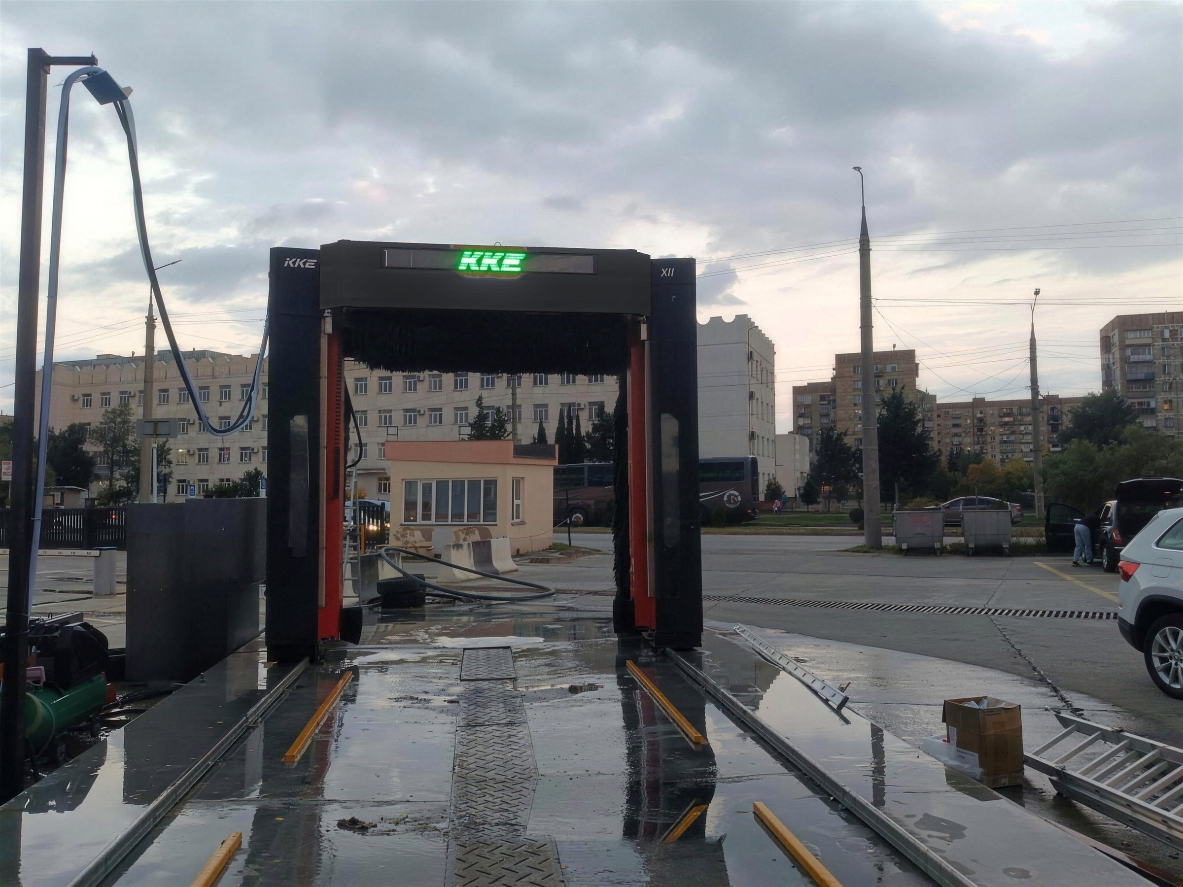 Looking down the bay of a KKE X1.1 installation — the steel floor rails set into the wet apron, the drag chain running in its centre channel, and the gantry standing over the far end with KKE lit across its beam