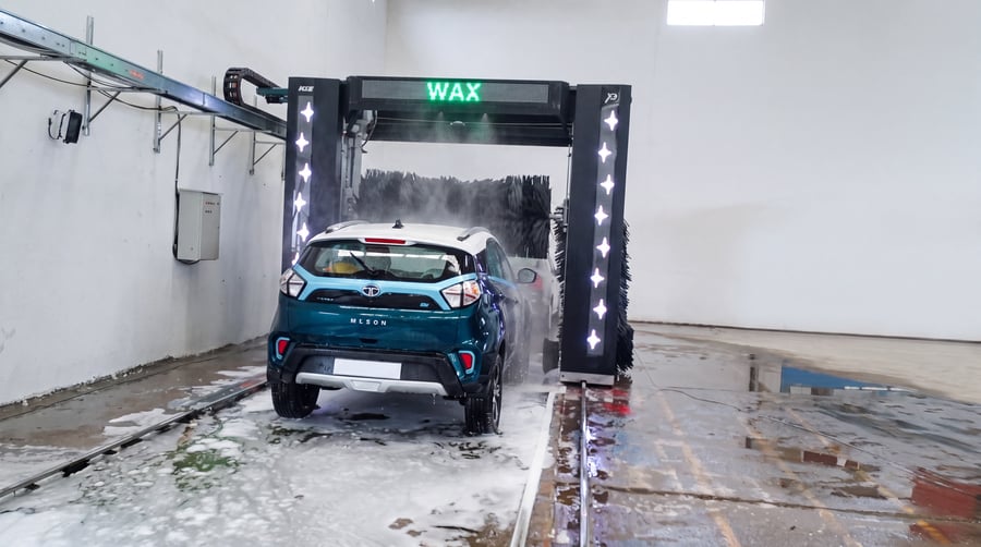 A rinsed teal SUV standing under a KKE X2 gantry, the beam display reading WAX and both column LED strips lit white