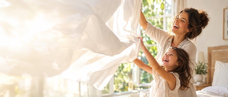 A mother and daughter laughing as they shake out a freshly laundered white sheet