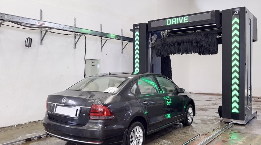 A dark saloon car on the rails of a KKE X2, the beam display reading DRIVE and both column LED strips running green chevron arrows