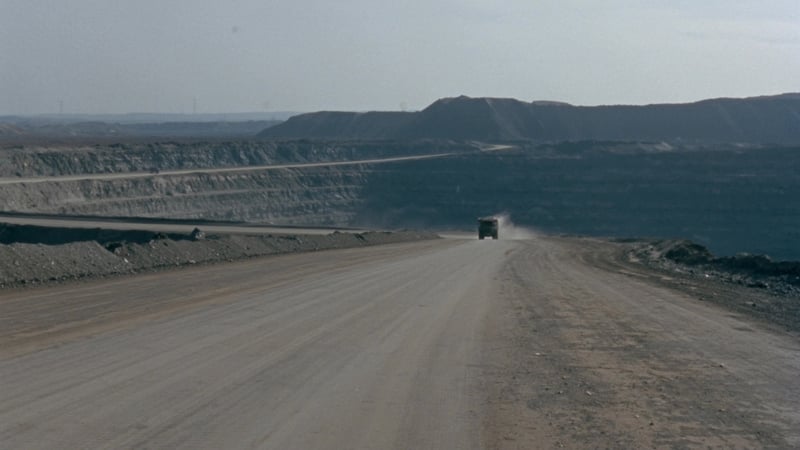 A wide compacted haul road climbing out of an open-pit mine, benched pit walls behind